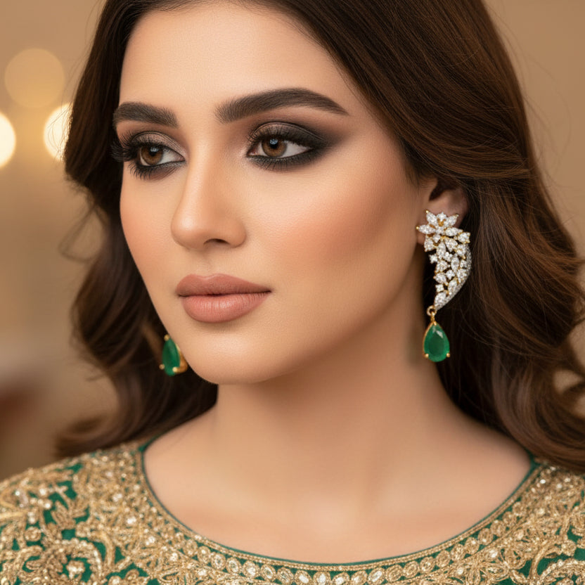 Pair of diamond earrings with green gemstones on a gray background, featuring the brand 'SAHELL'.