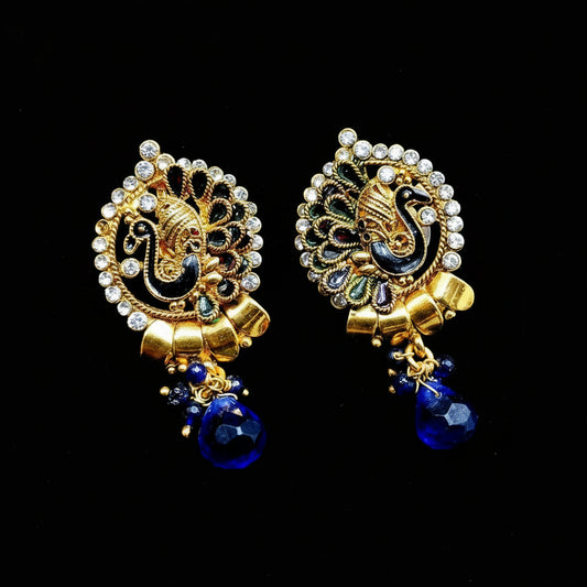 A pair of ornate gold-toned traditional earrings with black enamel detailing, white rhinestone borders, and dangling deep blue teardrop charms, shown on a black background with the brand name SAHELI MY BEST FRIEND at the top.