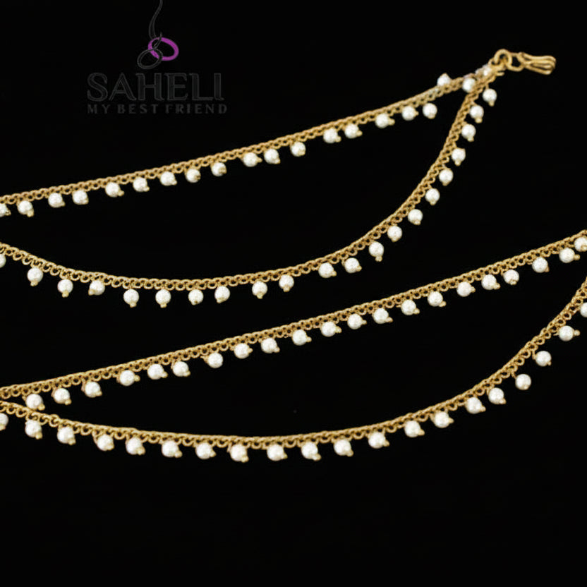 Two gold anklets with pearl beads on a dark background, branded 'SAHELI'.