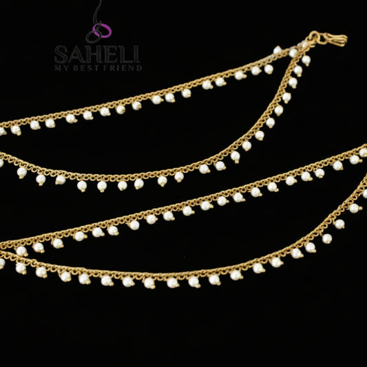 Two gold anklets with pearl beads on a dark background, branded 'SAHELI'.