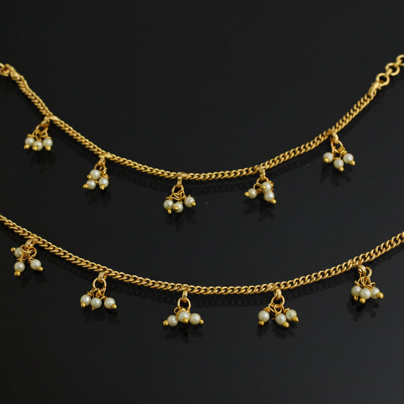 Gold anklets with pearl-like beads on a dark background
