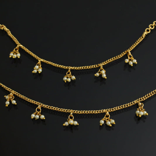 Gold anklets with pearl-like beads on a dark background