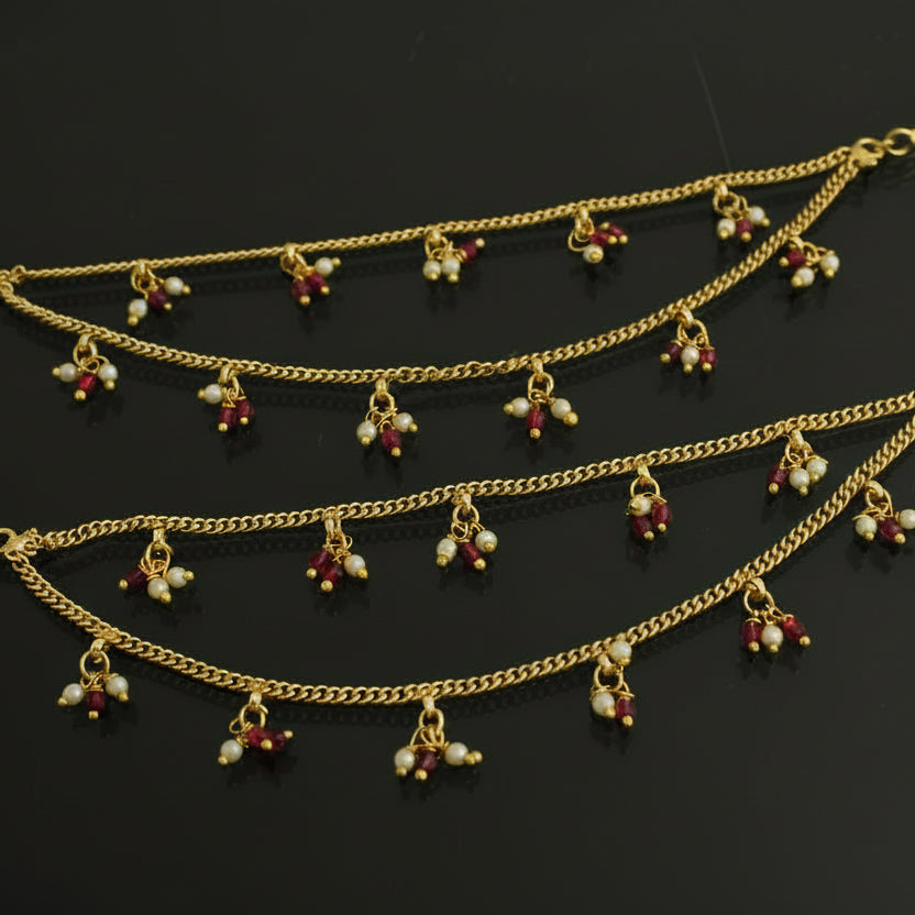 Gold anklets with red and green beads on a black background