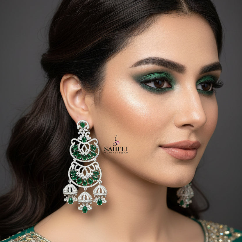 Pair of silver earrings with green gemstones on a gray background, branded 'Saheli'.