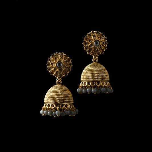Gold jhumka earrings on a gray stand with a blurred background