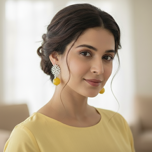 Woman wearing yellow earrings and a yellow top in a blurred indoor setting