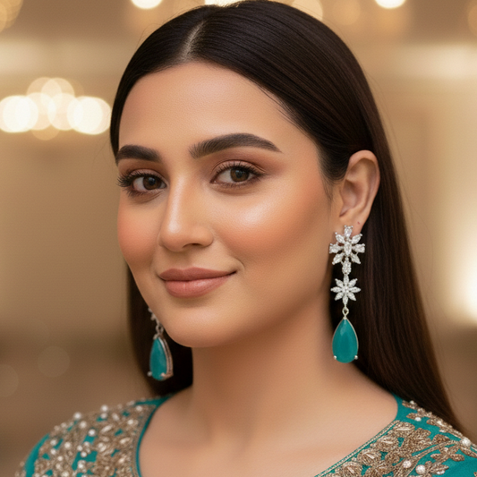 Woman wearing a teal and silver embroidered outfit with matching earrings against a blurred background.