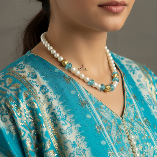 Necklace with white pearls, blue and gold beads on a gray background, featuring the brand 'Saheli'.