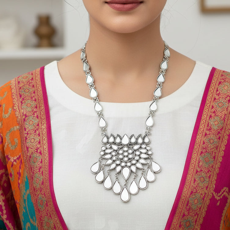 Silver necklace with white stones on a dark background, featuring the brand 'Saheli'.