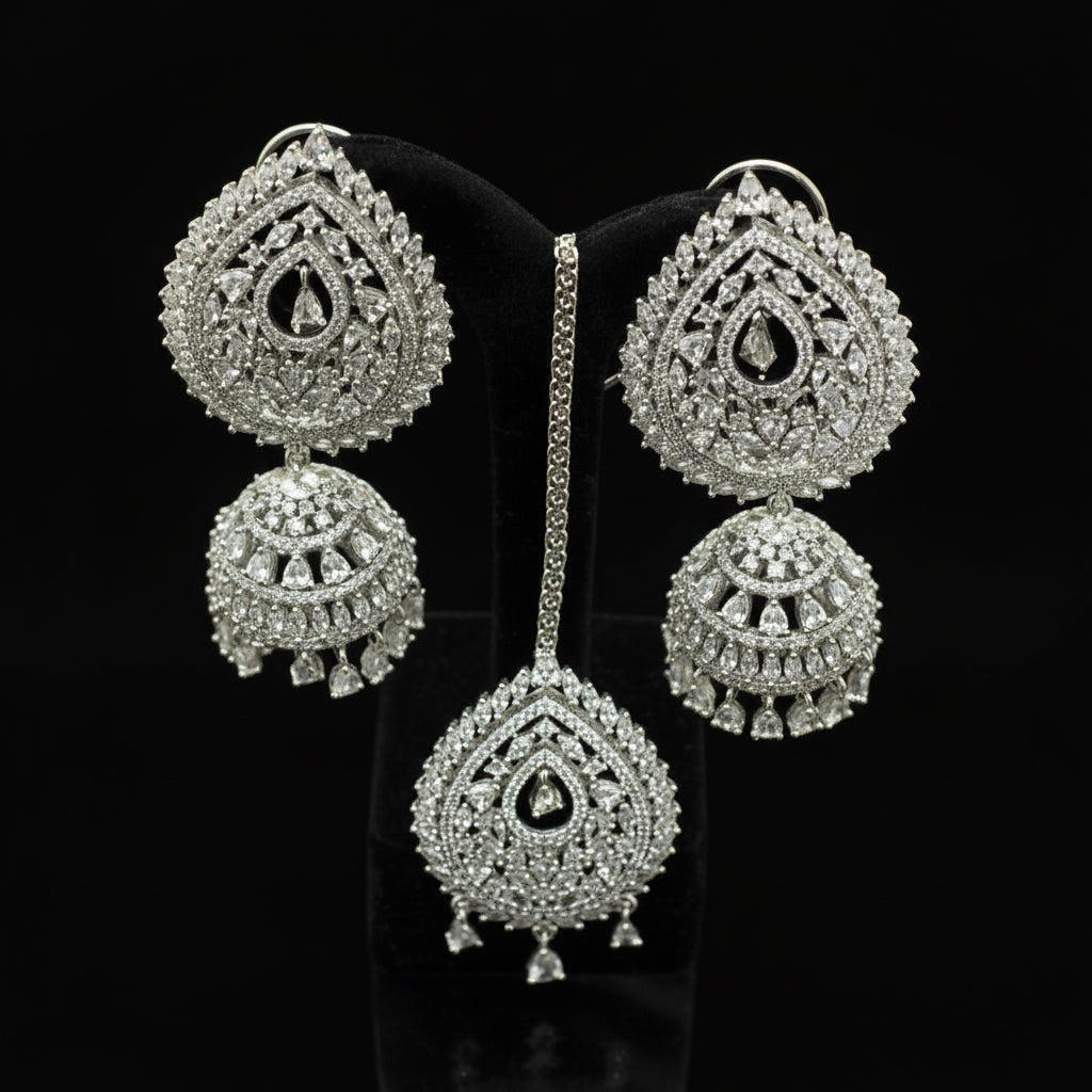 Silver earrings with intricate designs on a black stand, branded 'Saheli'.