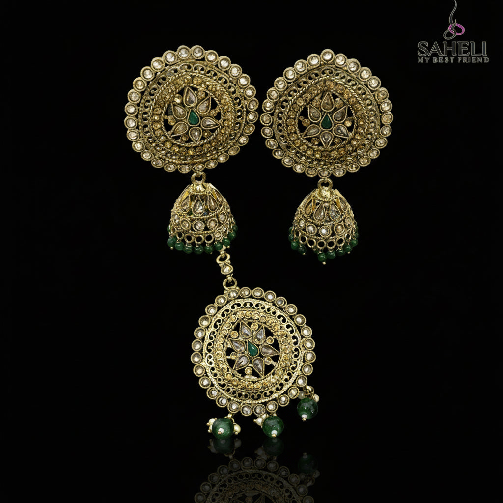 Ornate gold earrings with green stones on a dark stand, branded 'Saheli'.