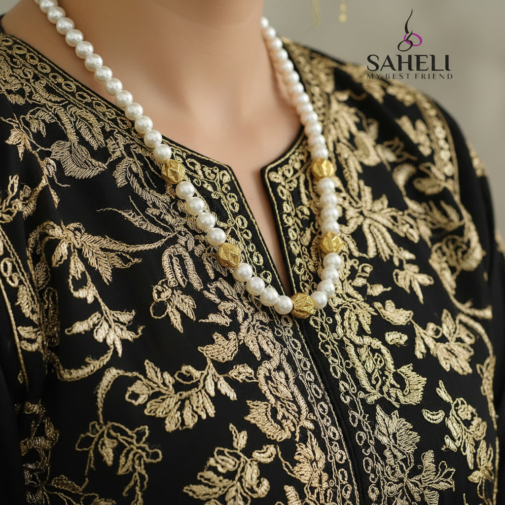 Pearl necklace with gold beads on a dark surface, featuring the brand 'Saheli'.