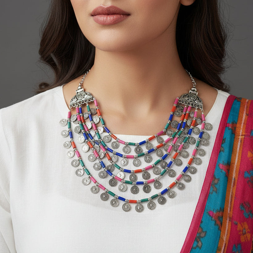 Colorful necklace with coins and beads on a dark background, featuring the brand 'Saheli'.