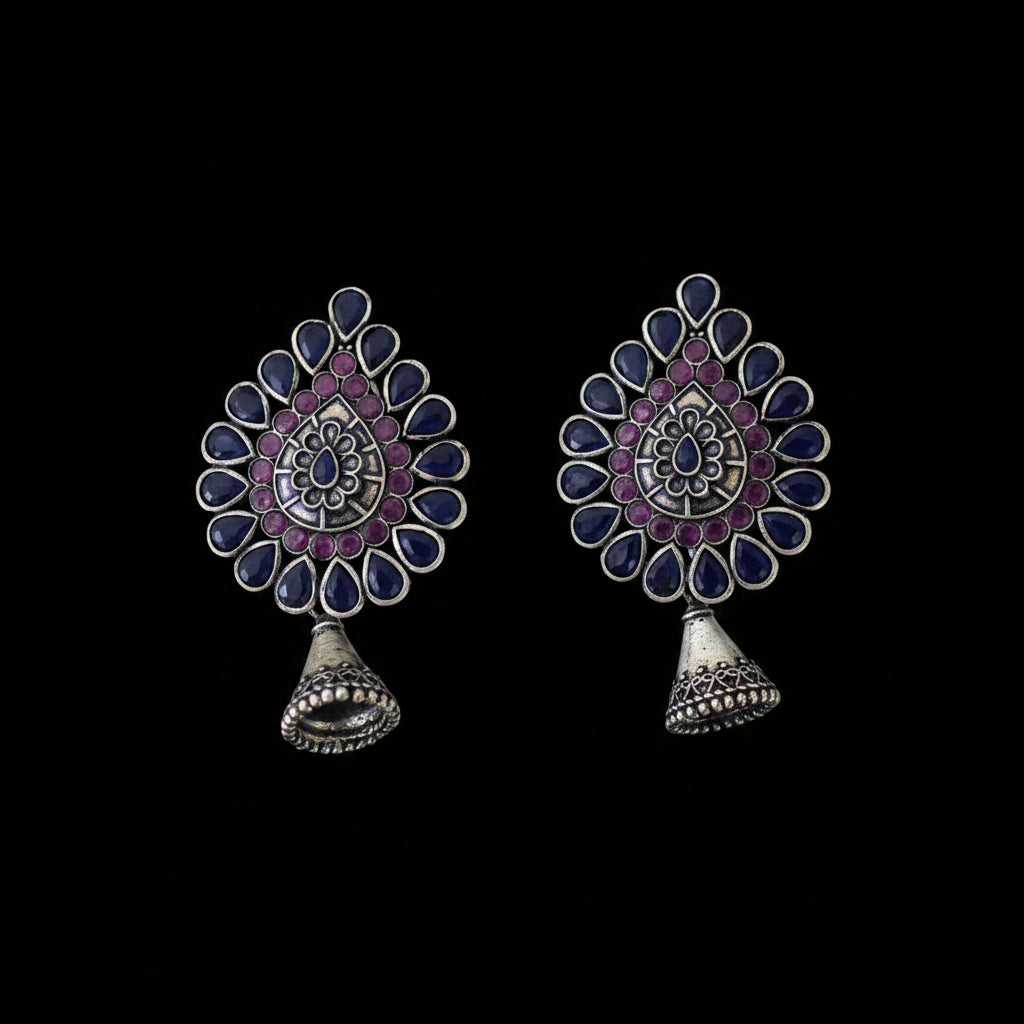 Pair of ornate earrings with purple and blue stones on a dark background, branded 'SAHELI'.