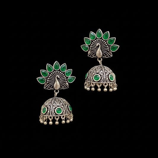 Ornate earrings with green accents on a gray stand, branded 'Saheli'.