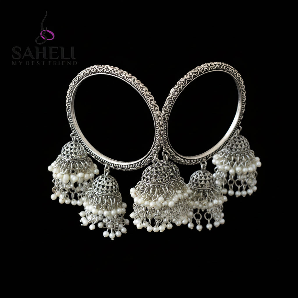 Silver and pearl earrings on a black stand with 'SAHELI' branding.