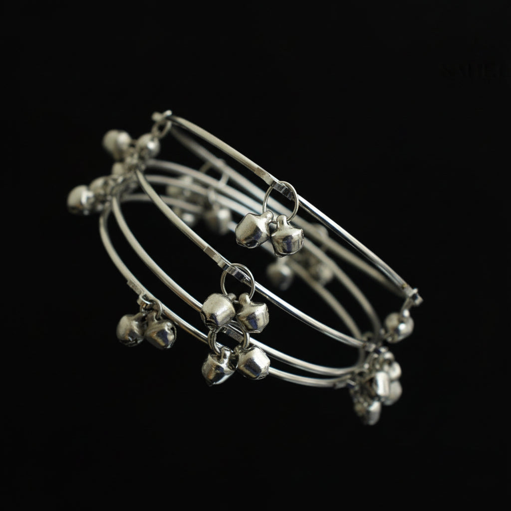 Set of silver anklets with small bells on a dark gray stand, brand 'Saheli' visible.