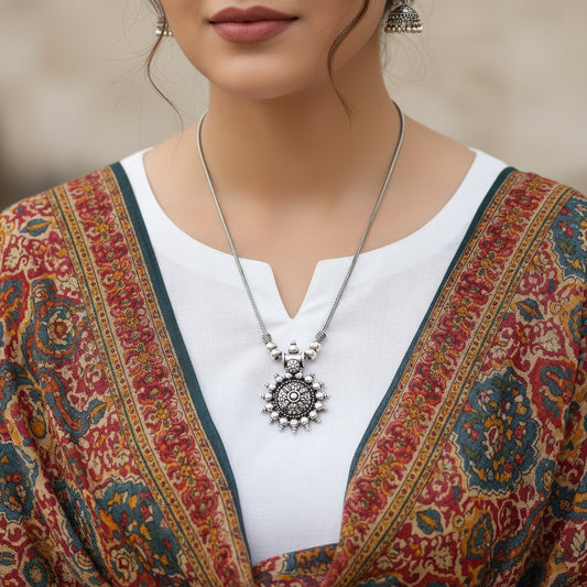 Silver necklace with a detailed pendant on a gray background, featuring the brand 'SAHELI'.