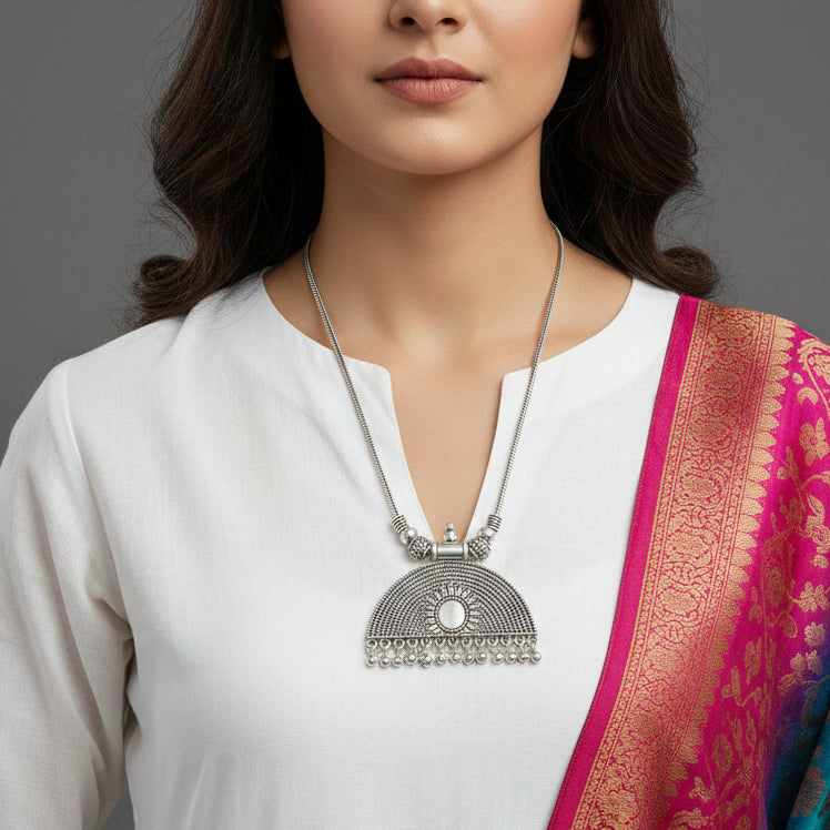 Silver necklace with a pendant on a gray background, featuring the brand 'Saheli'.