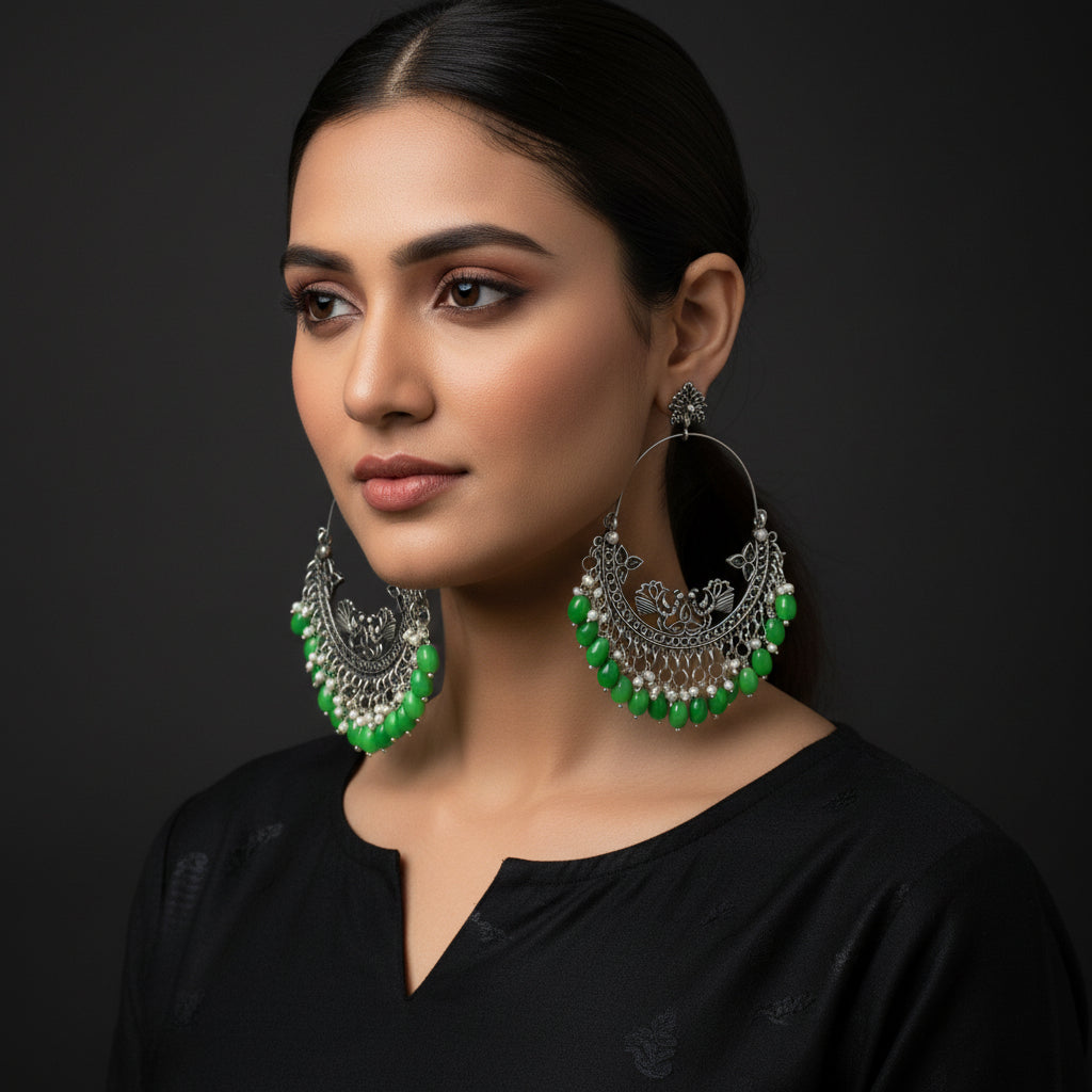 Ornate hoop earrings with green beads on a dark background