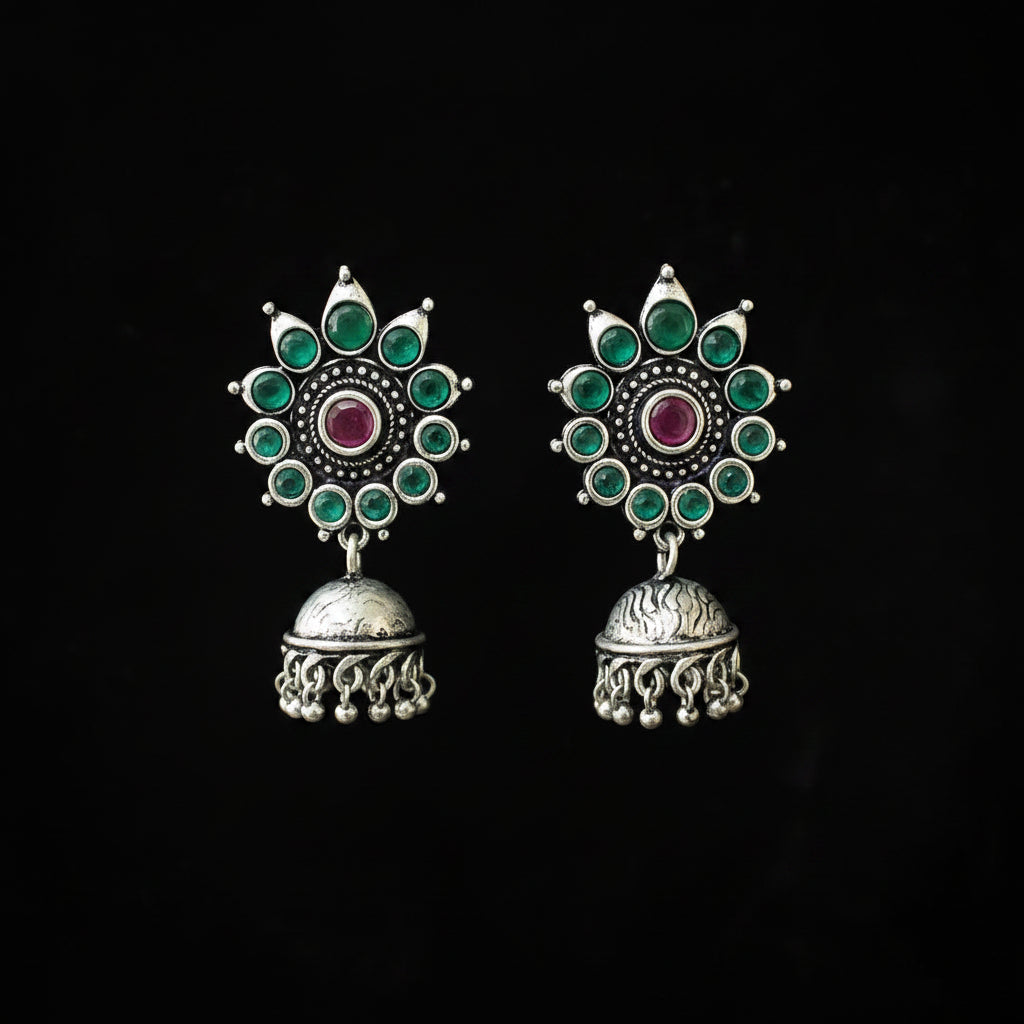 Ornate silver earrings with green and red stones on a black background