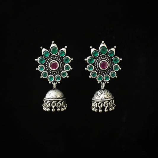 Ornate silver earrings with green and red stones on a black background