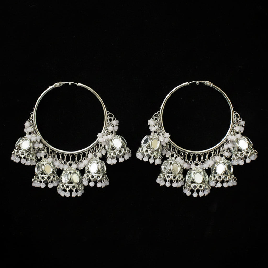 A pair of silver-toned traditional Indian jhumka hoop earrings with intricate filigree work, small white bead chains, and circular mirror embellishments, displayed against a solid black background.