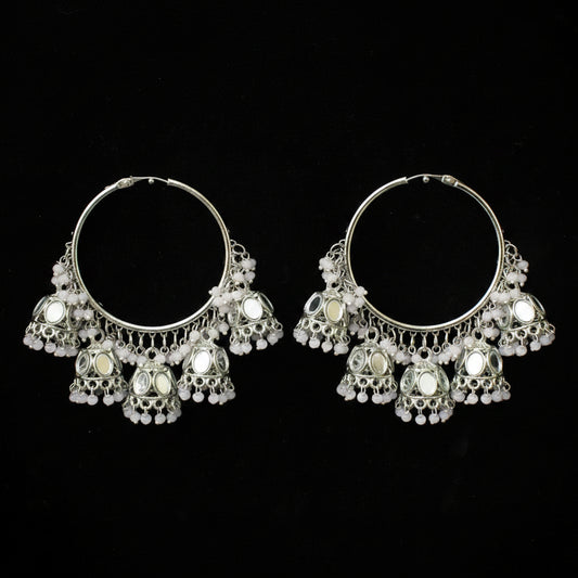 A pair of silver-toned traditional Indian jhumka hoop earrings with intricate filigree work, small white bead chains, and circular mirror embellishments, displayed against a solid black background.