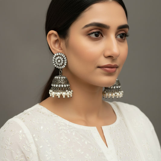 Silver and pearl earrings on a gray stand with 'Saheli' branding.