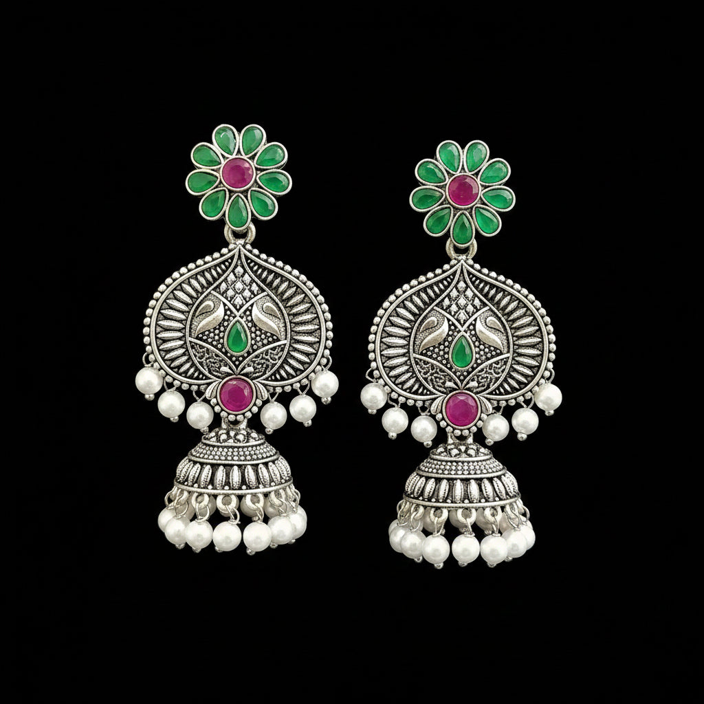 Ornate earrings with green, pink, and white stones on a gray stand.