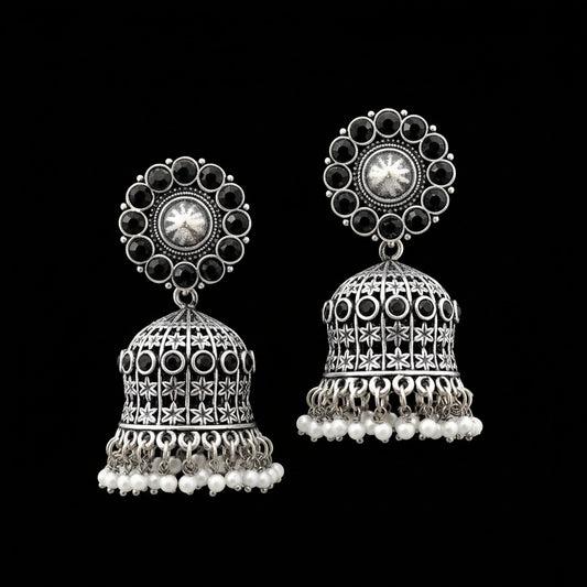 Pair of silver jhumka earrings with black stones and pearl accents on a gray stand.