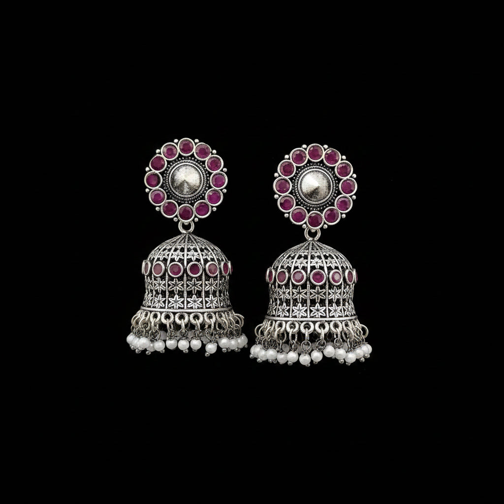 Silver jhumka earrings with pink gemstones on a gray stand.