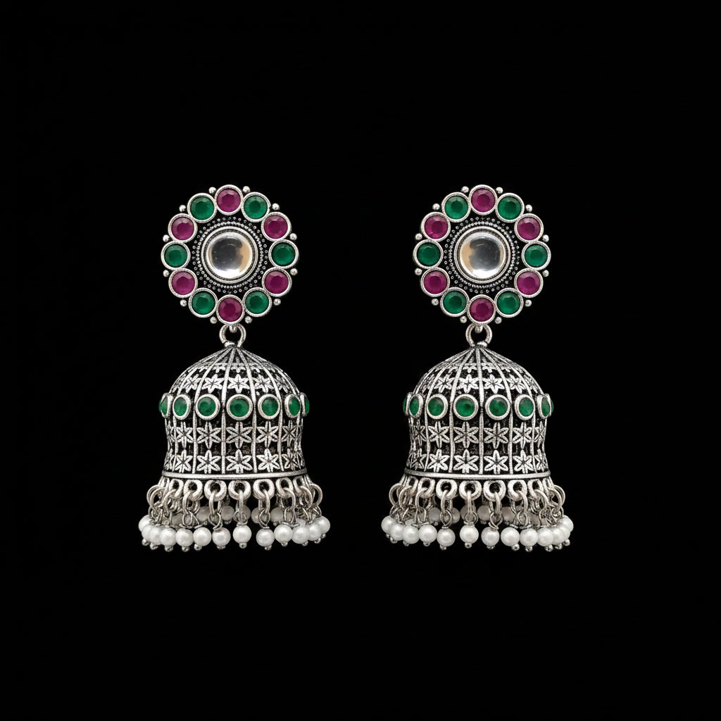 Pair of silver jhumka earrings with colorful gemstones and pearl accents on a gray stand.