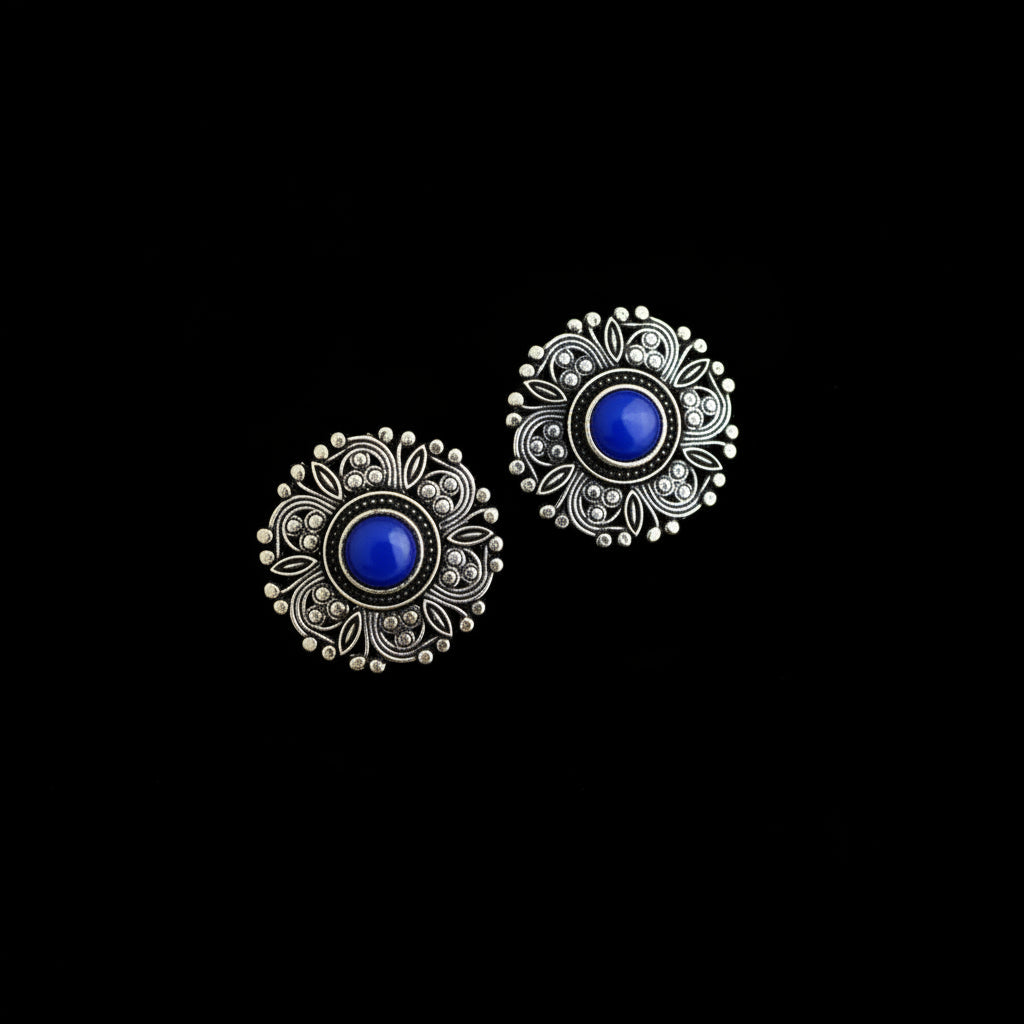 A pair of ornate silver-toned filigree earrings with round black stone centers, displayed on a dark reflective surface.