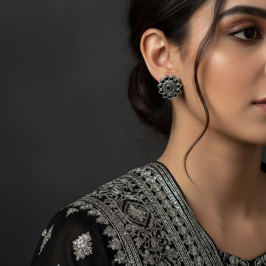 A pair of silver-toned circular earrings with black circular details, displayed on a dark reflective surface.