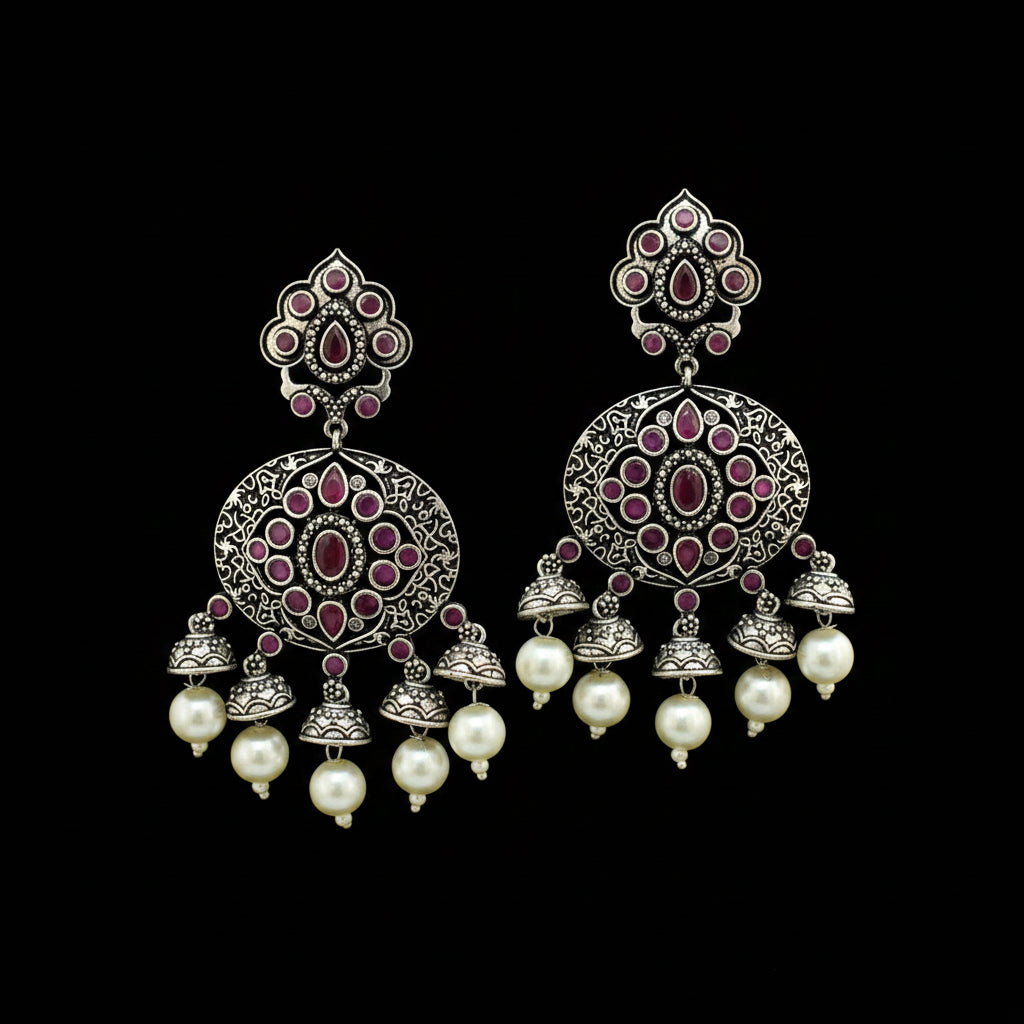 A pair of ornate silver-toned Indian jhumka earrings with pink stone accents and white pearl drops, displayed on a black Y-shaped stand against a gray background with an HP logo partially visible.