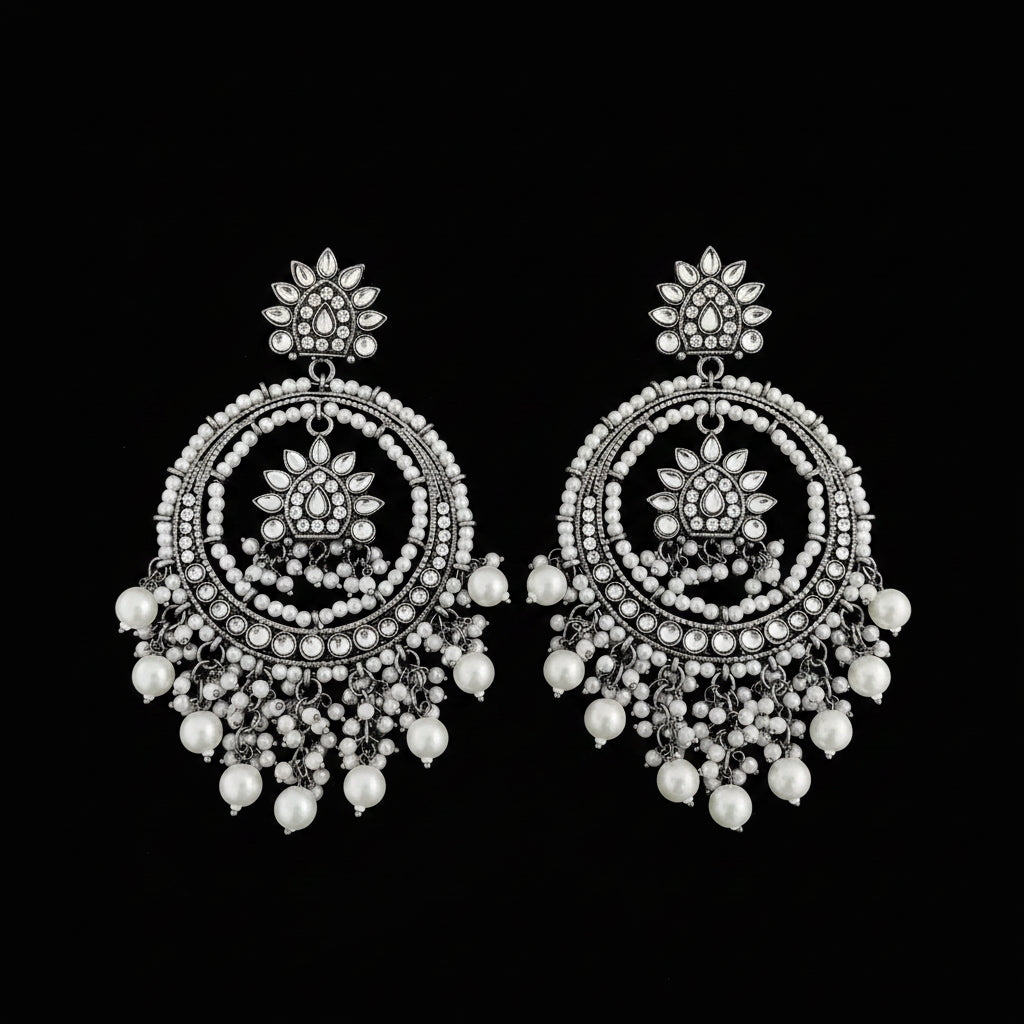 A pair of ornate silver-toned dangle earrings with intricate circular beadwork, floral motifs, and dangling pearl-like beads, displayed on a dark reflective surface.