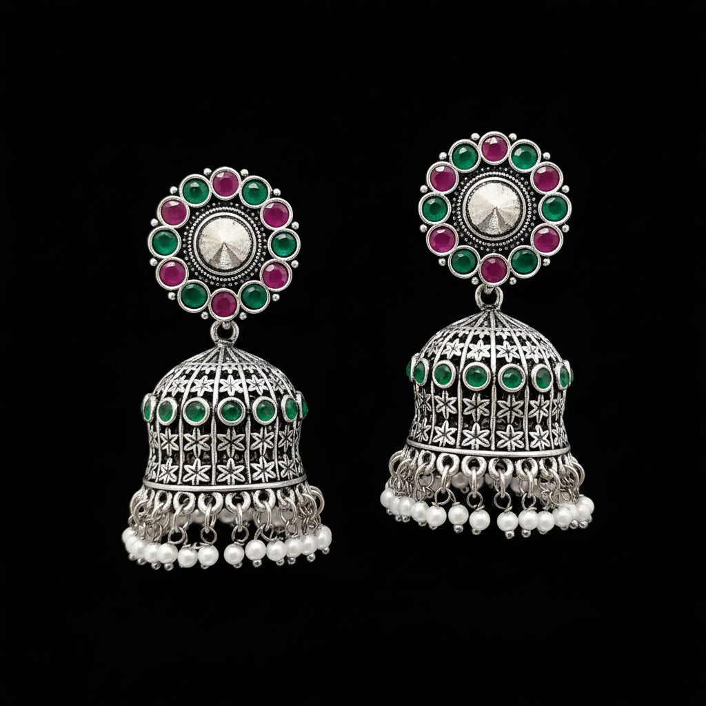 Pair of silver jhumka earrings with colorful gemstones and pearl accents on a gray stand.