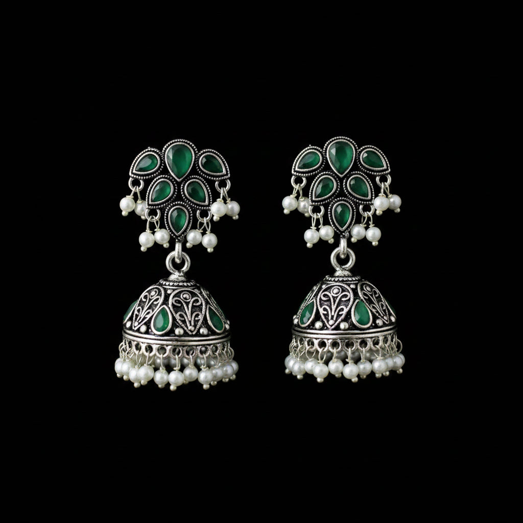 A pair of silver-toned Indian jhumka earrings with green enamel and white pearl bead accents, displayed on a black jewelry stand.