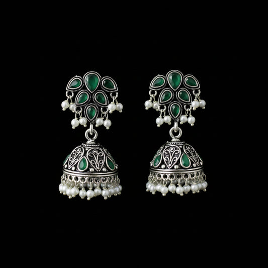 A pair of silver-toned Indian jhumka earrings with green enamel and white pearl bead accents, displayed on a black jewelry stand.