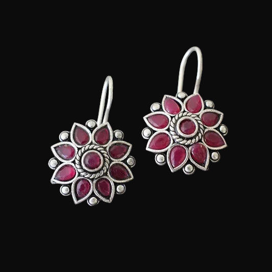 Pair of silver earrings with red gemstones on a gray stone surface