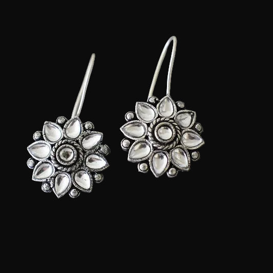 Pair of silver floral earrings on a gray cushion with a dark background