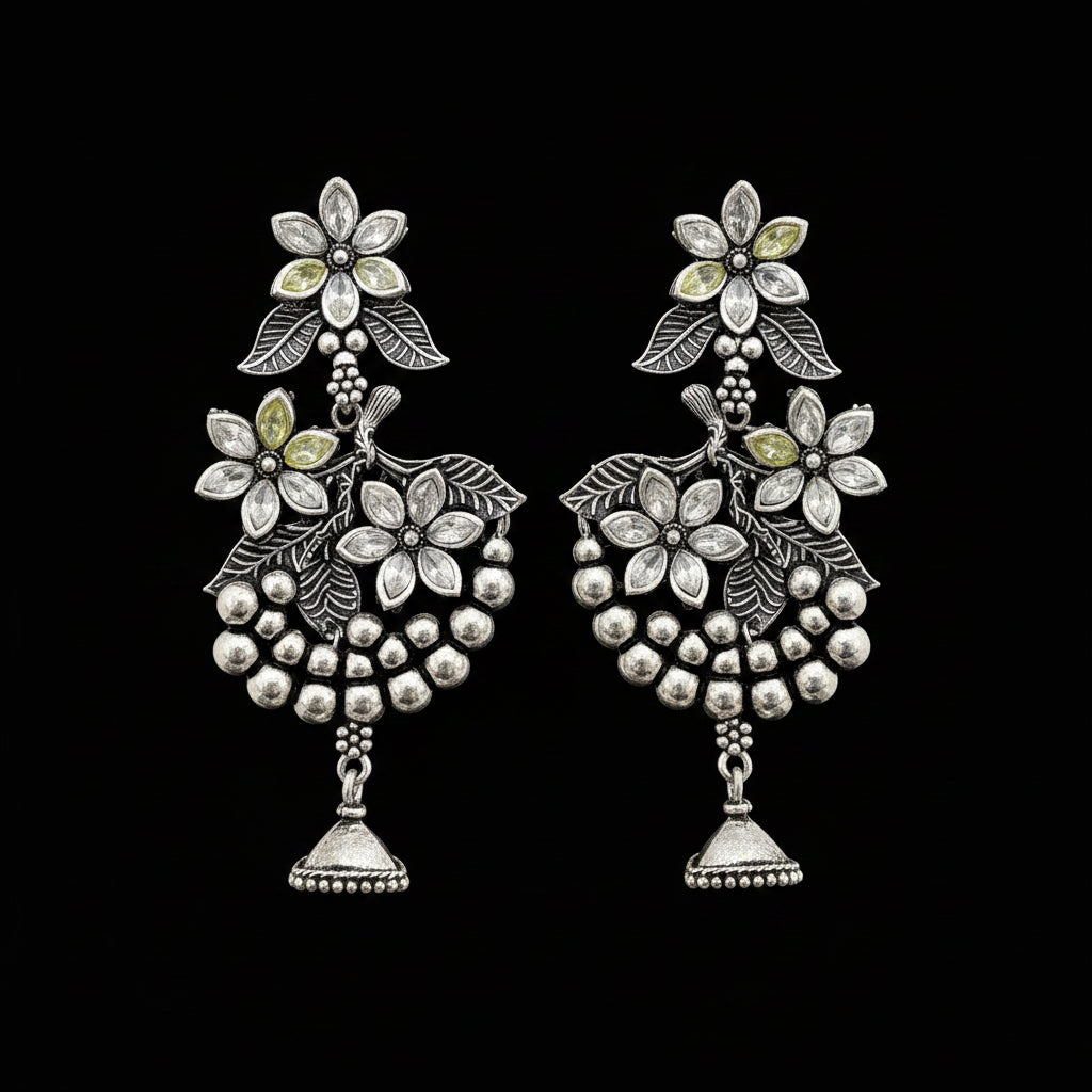 Silver floral earrings on a gray stand with 'Saheli' branding.