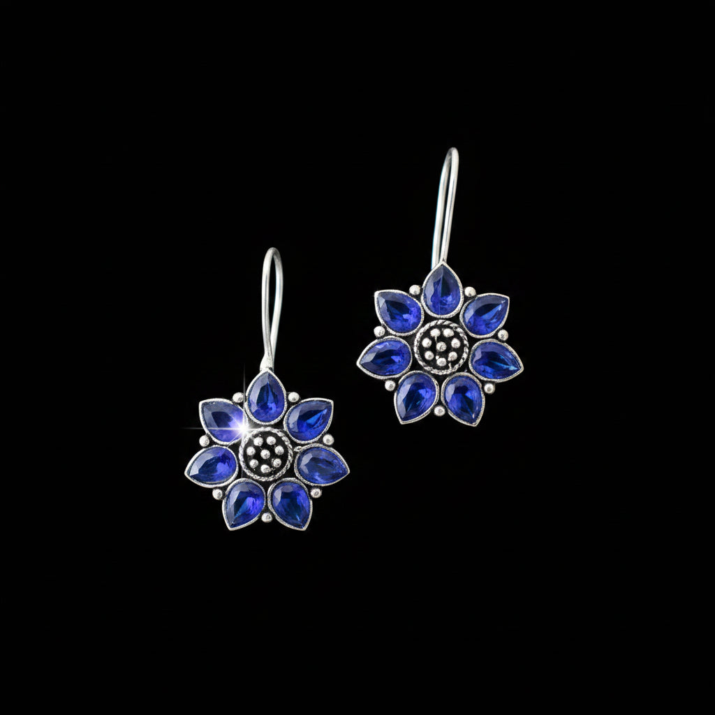 Pair of blue flower-shaped earrings on a gray cushion with a gray background