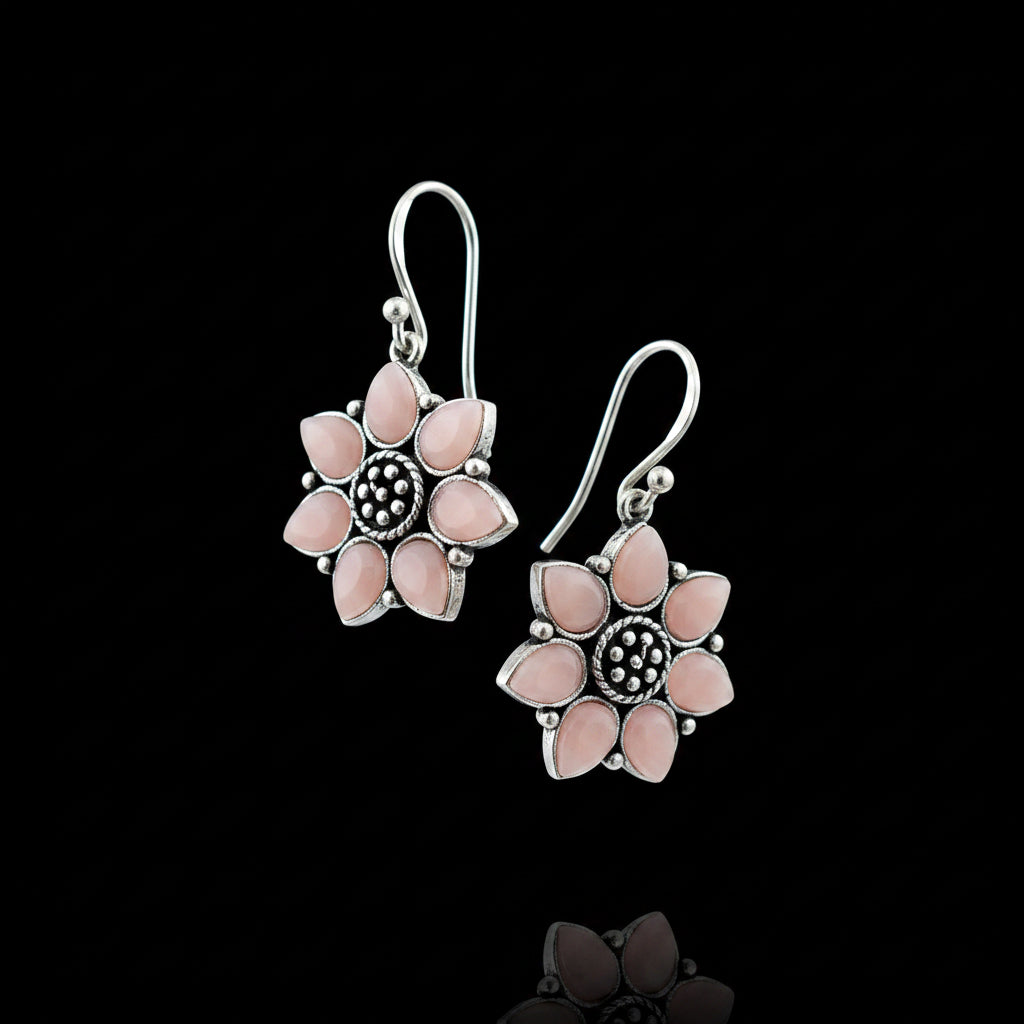 Flower-shaped earrings with pink petals and silver accents on a gray cushion.