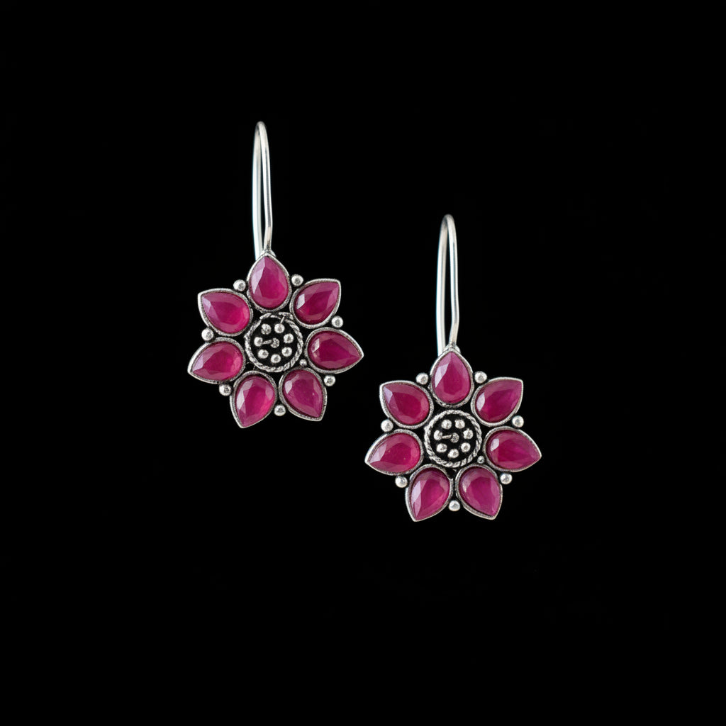 Flower-shaped earrings with pink petals and silver centers on a gray cushion.