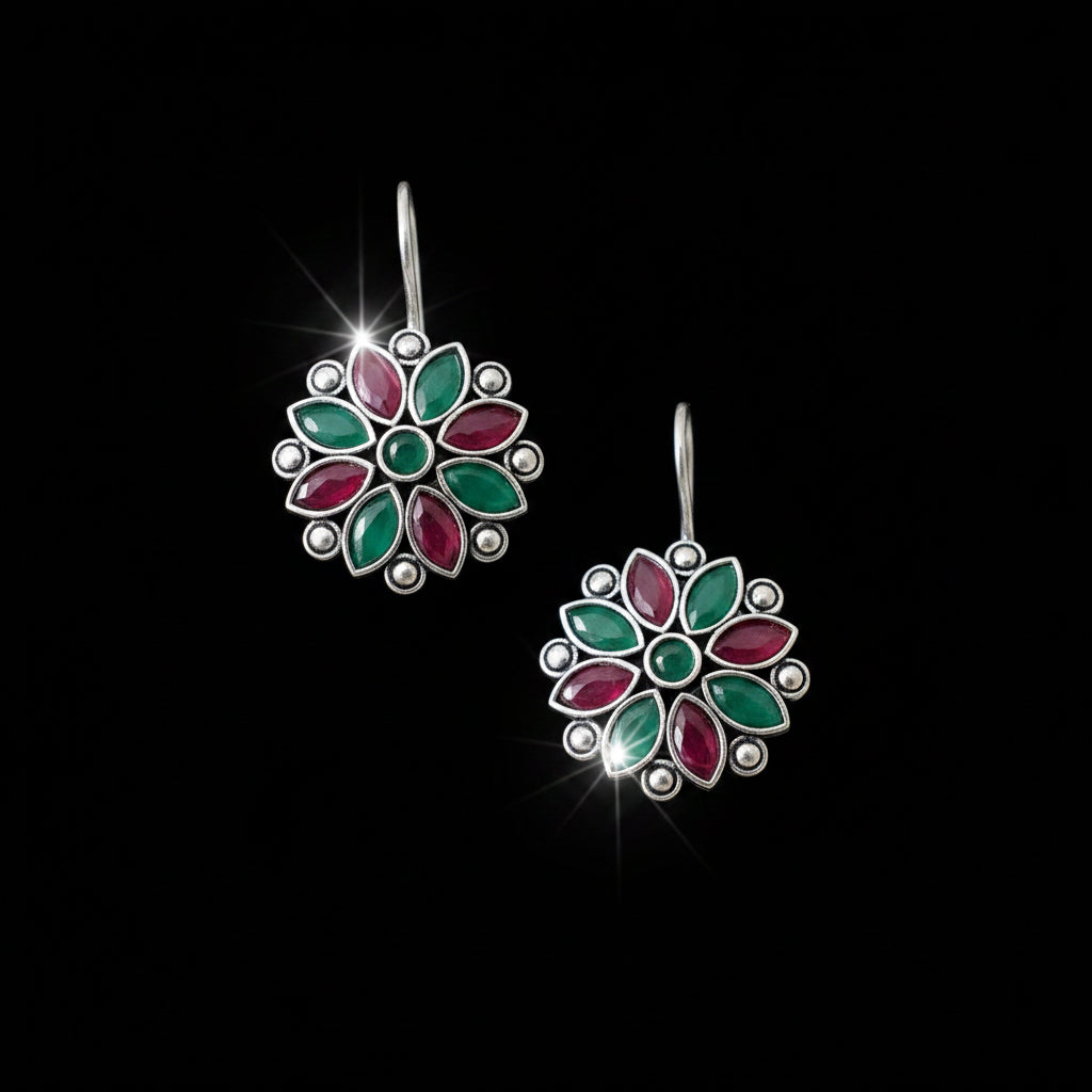 Floral earrings with red and green stones on a gray surface