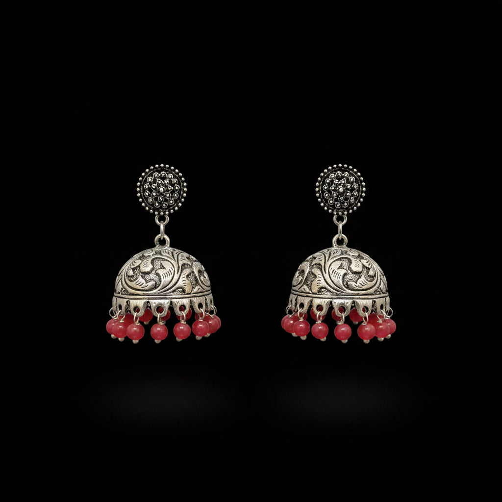A pair of traditional Indian silver jhumka earrings with red bead drops, displayed on a gray velvet stand. The brand logo 'SAHELL MY BEST FRIEND' is visible at the top center.