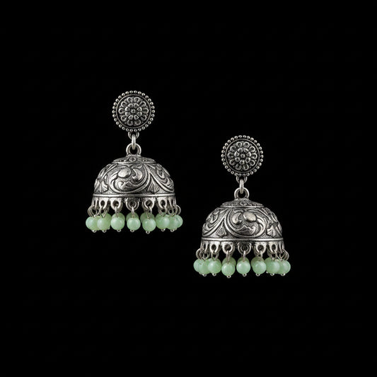 A pair of traditional Indian silver-toned jhumka earrings with green bead tassels, displayed on a gray velvet stand. The brand logo 'SAHELI MY BEST FRIEND' is visible at the top center.
