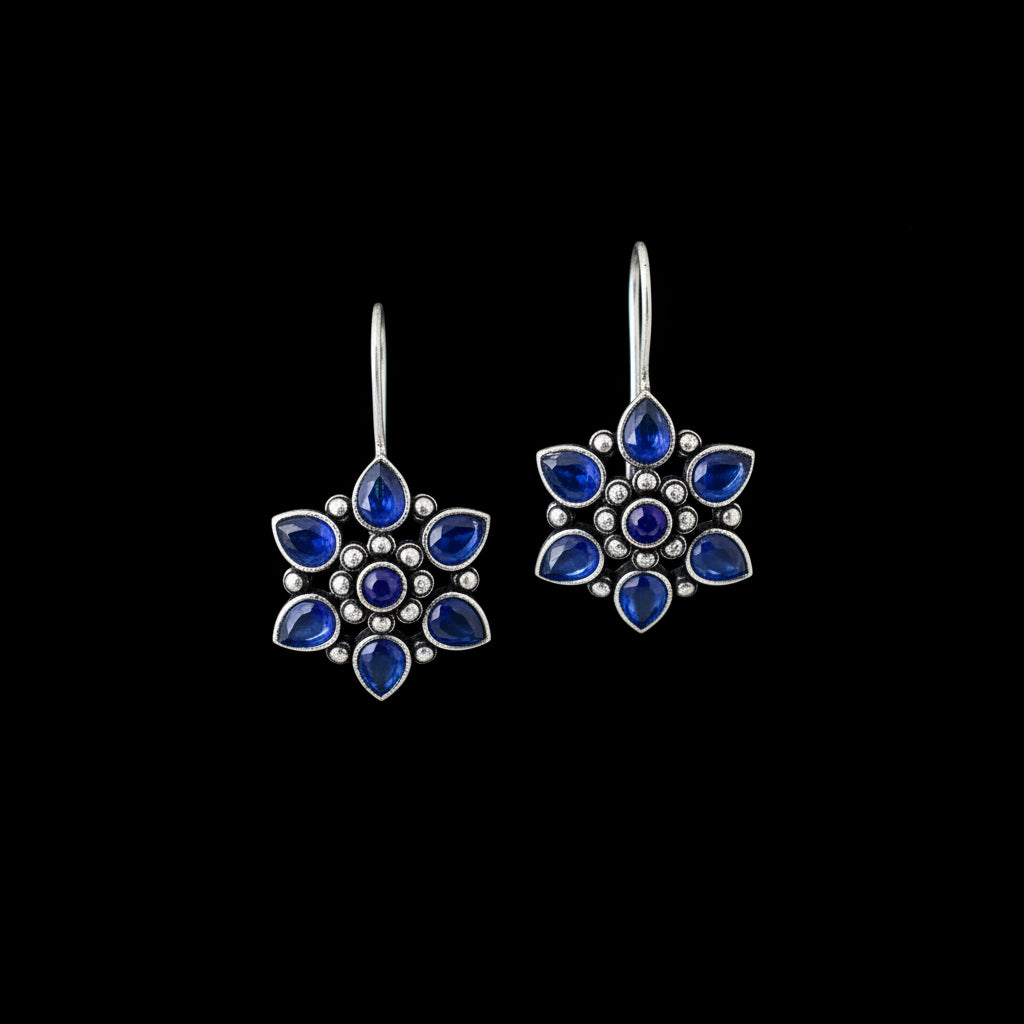 A pair of silver-toned dangle earrings with blue gemstone clusters, displayed on a gray velvet jewelry cushion against a neutral gray background.
